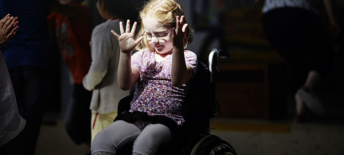 Ein Mädchen sitzt im Rollstuhl, ein Lichtstrahl ist auf sie gerichtet.